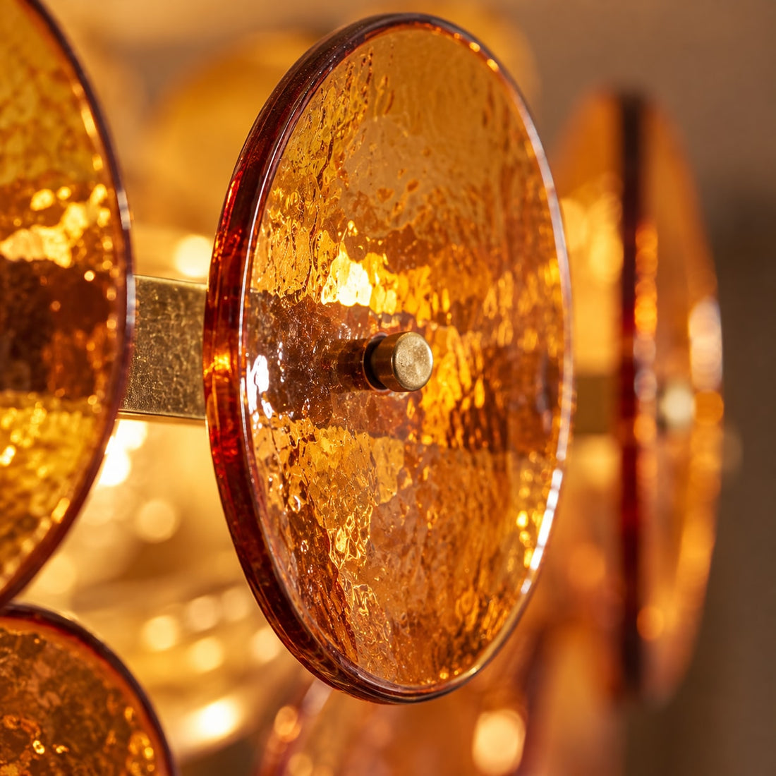Kronleuchter mit Bernstein-Glasscheiben, Ø 60–100 cm – Nahaufnahme: die Aufhängung einer Glasscheibe am goldfarbenen Gestell mit Öse